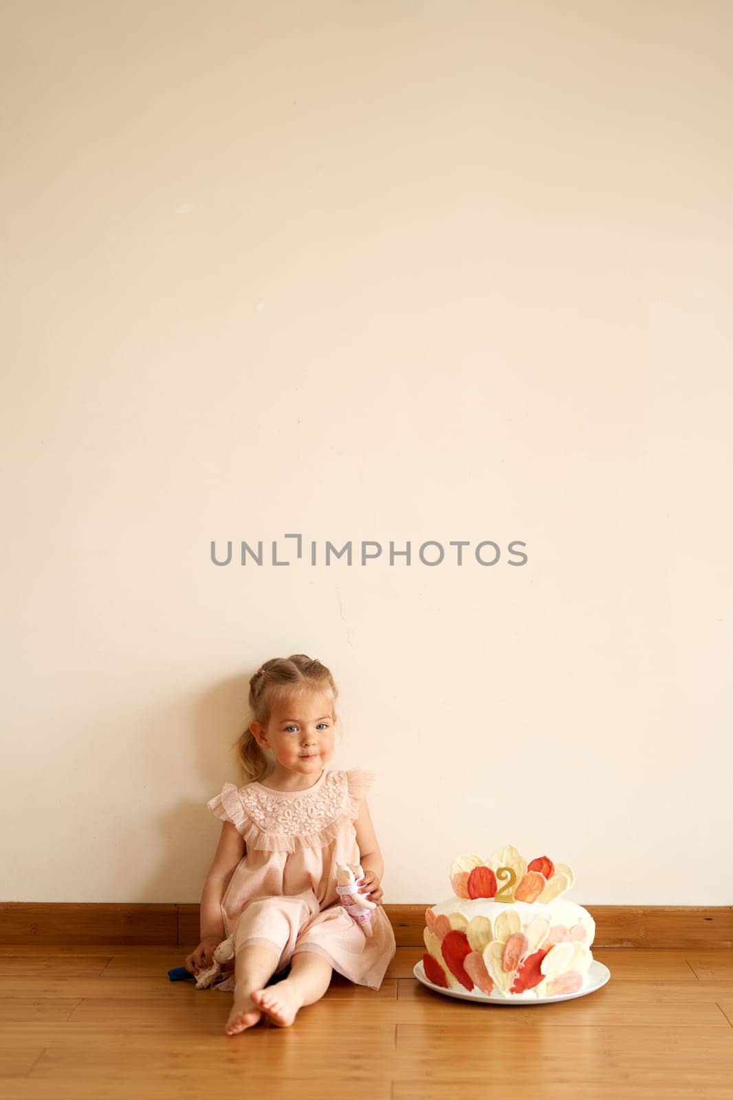 Little smiling girl with a doll sits on the floor next to a birthday cake. High quality photo