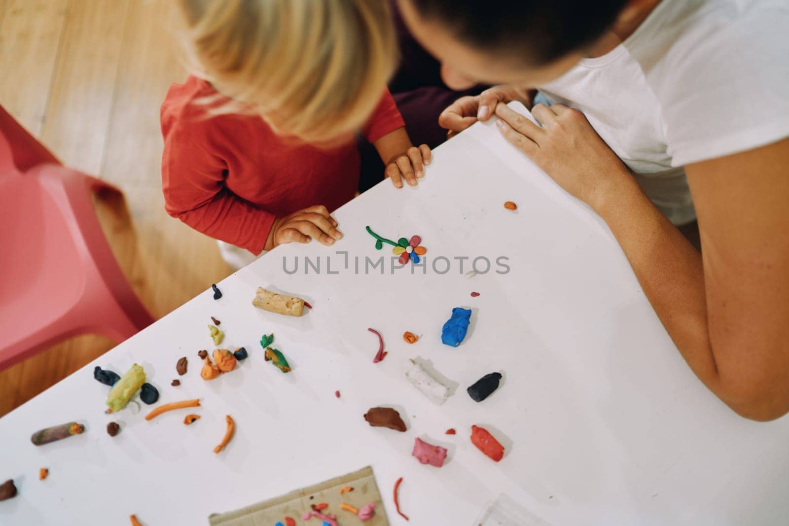 Mom with a little girl are looking at a plasticine flower on the table. Top view by Nadtochiy