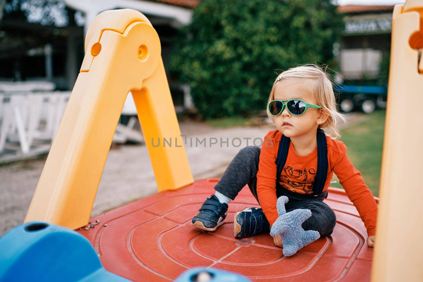 Little girl sits on a slide with a soft toy in her hand and looks into the distance. High quality photo