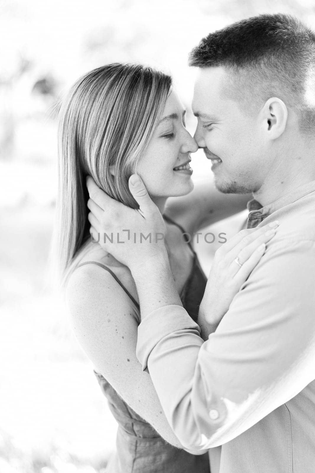 Smiling man hugs woman face and almost kisses her. Portrait. Black and white photo by Nadtochiy