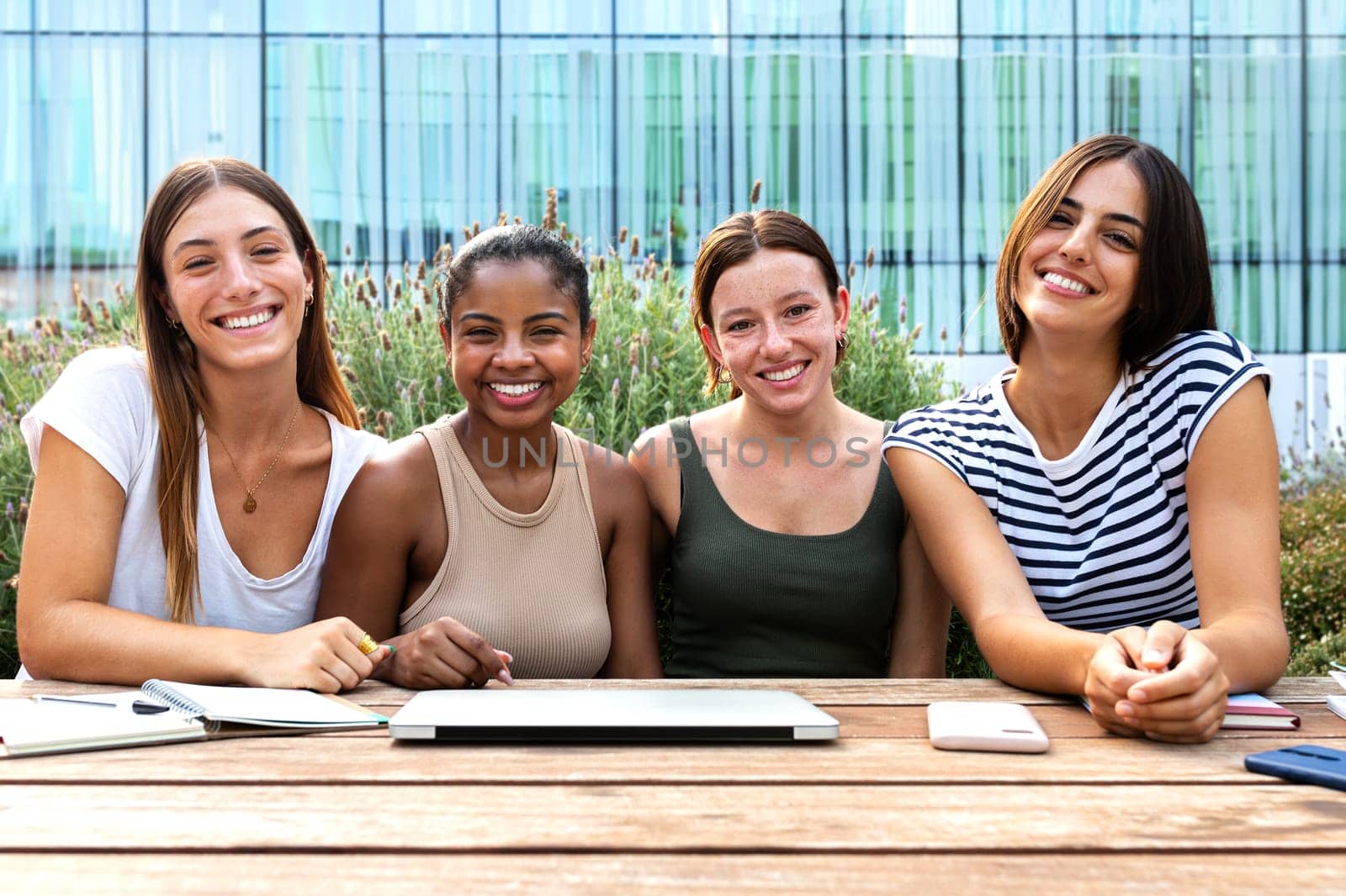 Front view of happy multiracial female university student friends studying outdoor in college campus looking at camera. by Hoverstock