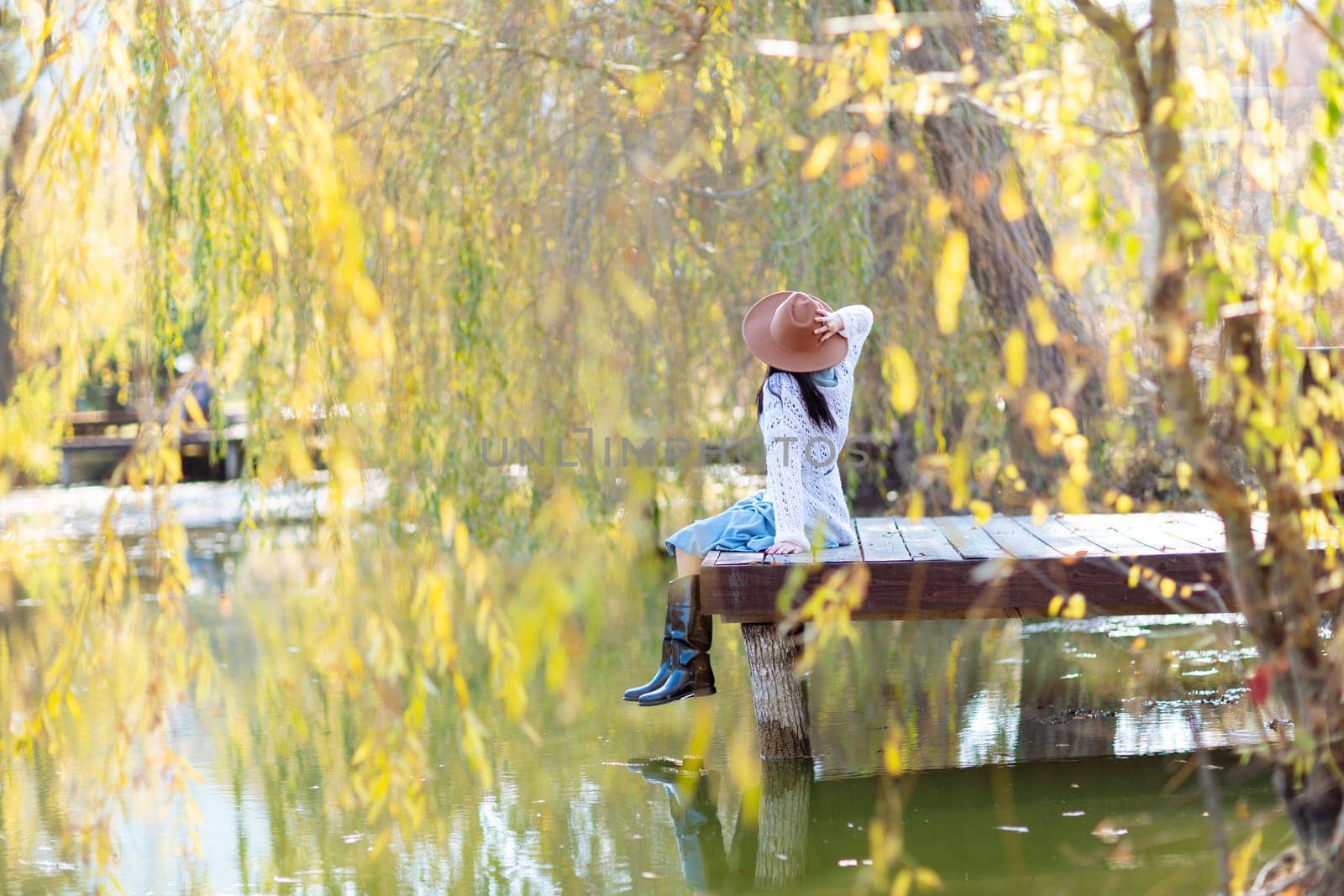 Autumn lake woman. She sits by a pond on a wooden pier in autumn and admires nature. The concept of tourism, weekends outside the city