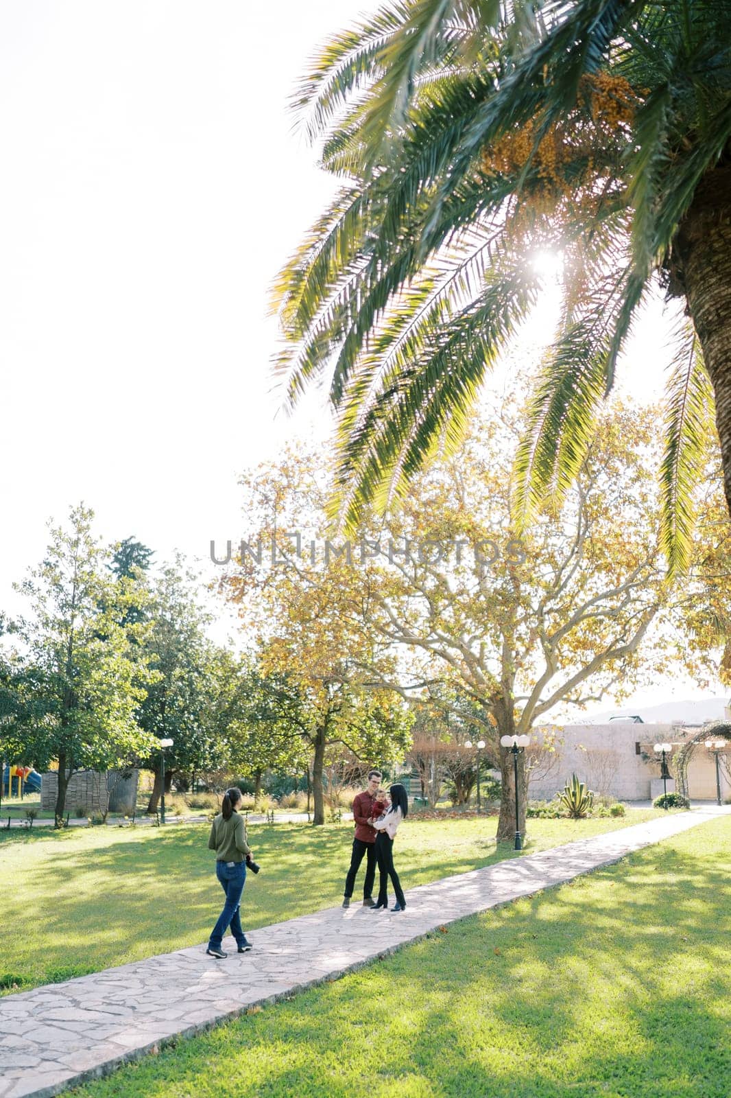 Girl-photographer walks along the path in the park to parents with a child. High quality photo