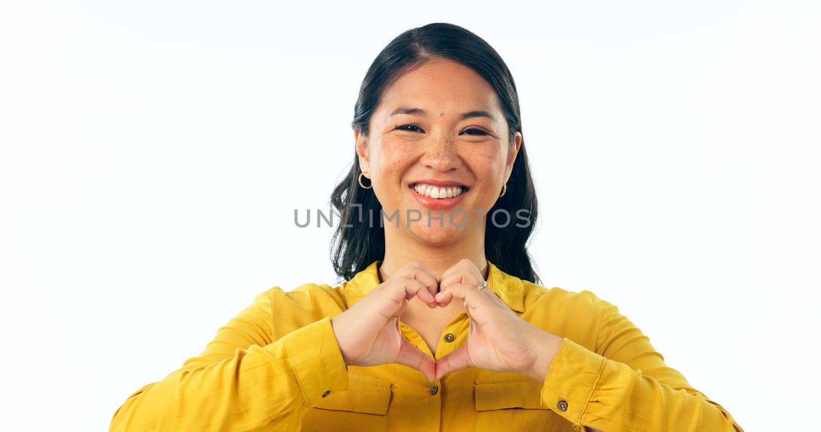 Portrait, smile and heart hands with a young asian woman isolated on a white background in studio for love or health. Face, emoji and romance with a happy young korean girl on valentines day by YuriArcurs