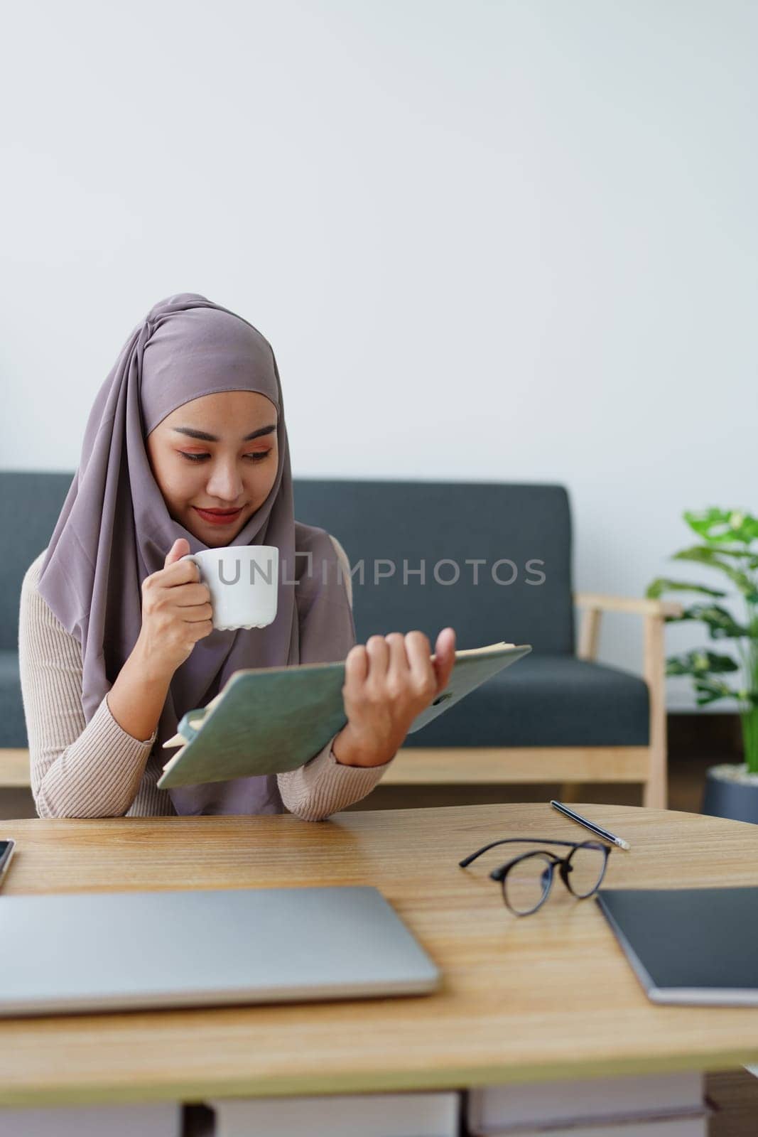 Muslim undergraduate student drinks coffee while read studying at home. by Manastrong
