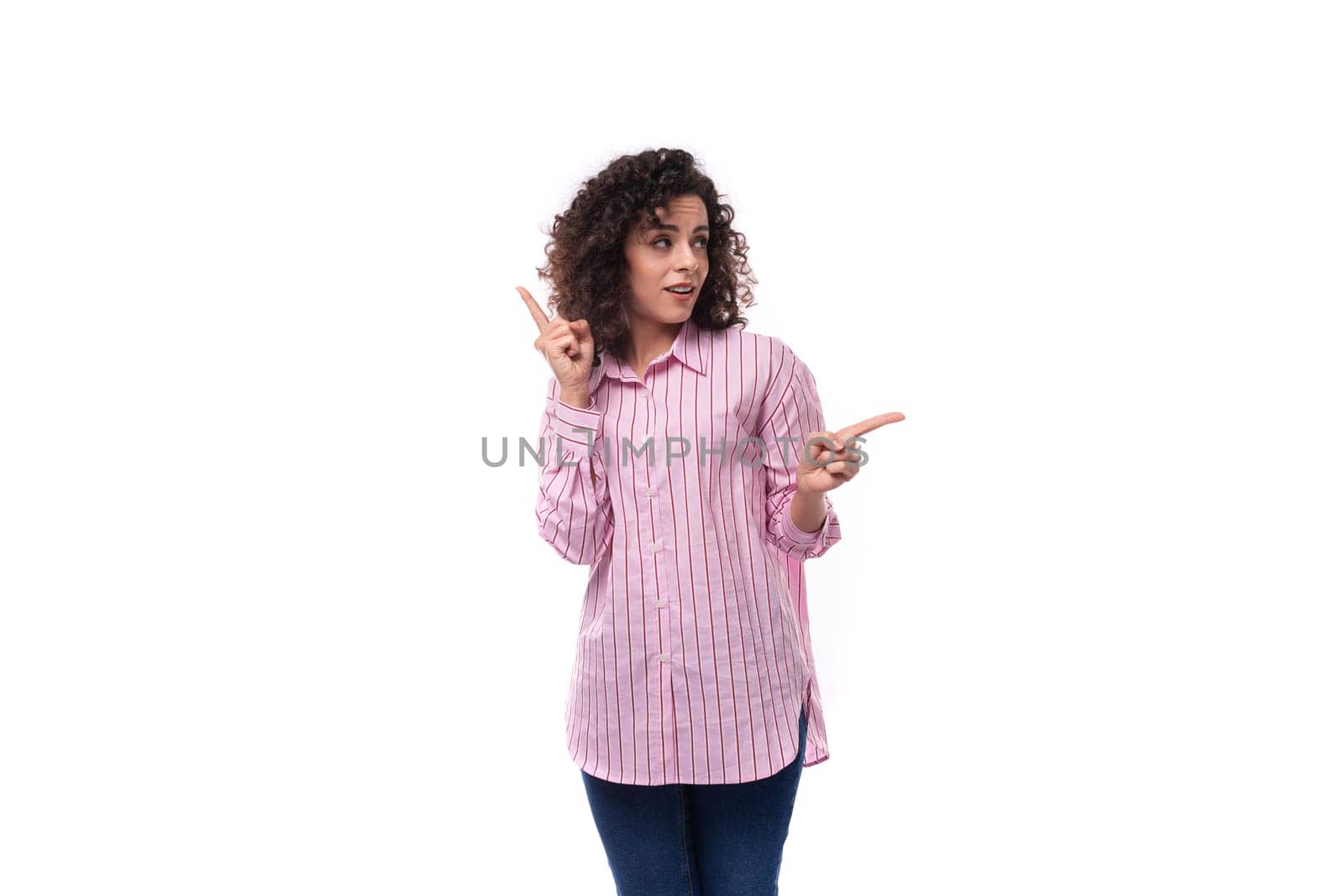 young authentic caucasian woman with curly black hair dressed in a pink shirt on a white background with copy space.