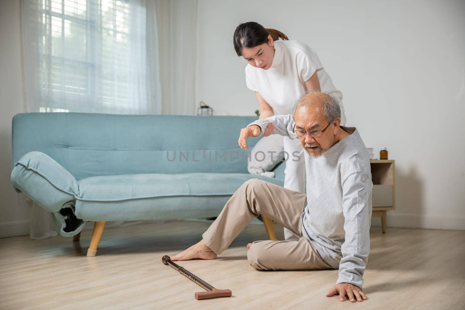 Asian elderly old man with walking stick fall on ground and granddaughter camp to help to support at home in living room, young woman halping her grandfather after falling down on floor, dizziness