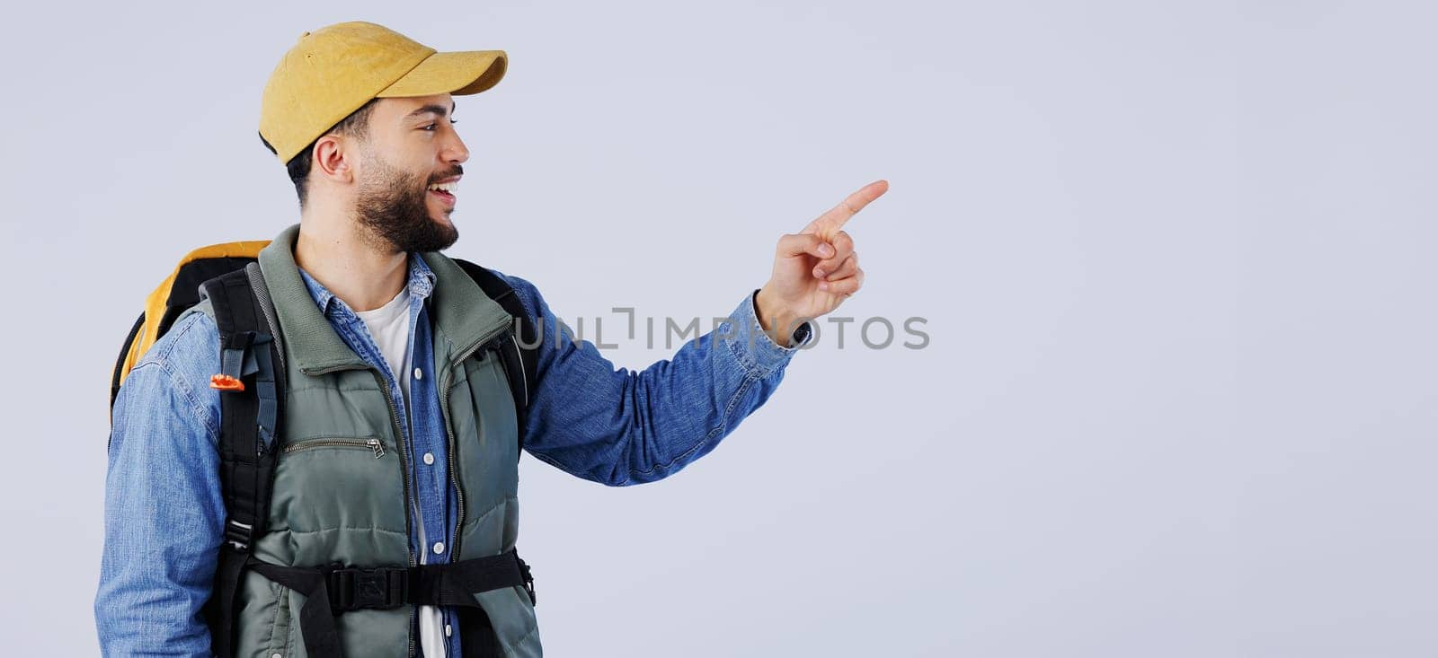 Happy man, backpack and pointing on mockup for hiking, adventure or travel tips against a studio background. Male person, model or hiker smile with bag showing trekking list, deal or advertising.