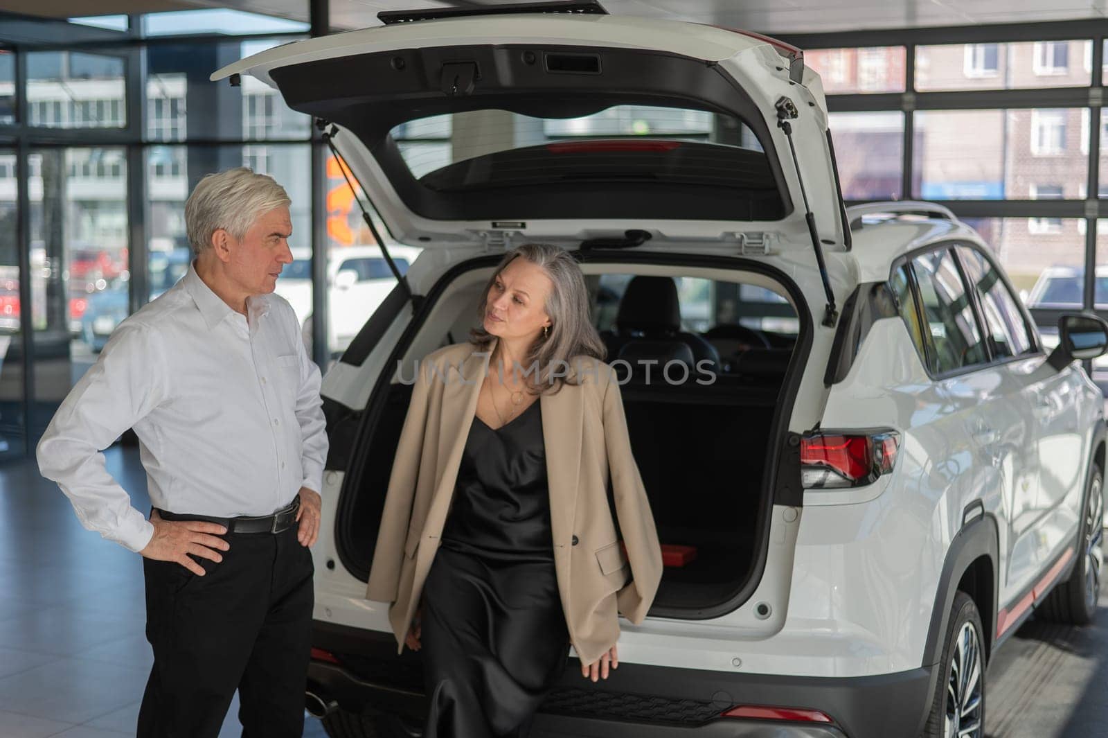 Mature Caucasian couple choosing a car looks at the trunk. by mrwed54