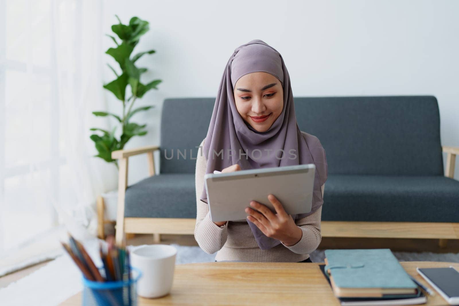 Female Muslim employee uses tablet to work at office. by Manastrong