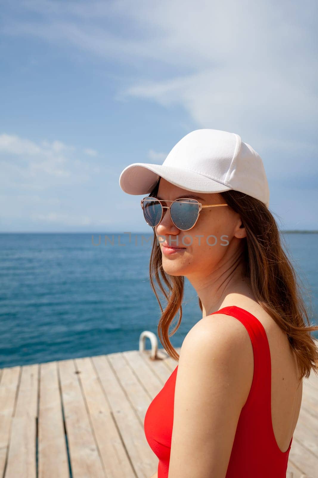 A beautiful girl with long hair and a white cap looks at the blue sea by AnatoliiFoto