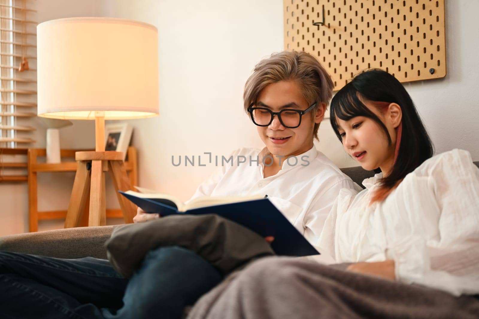 Relaxed young Asian couple reading book and spending weekend time together at home.