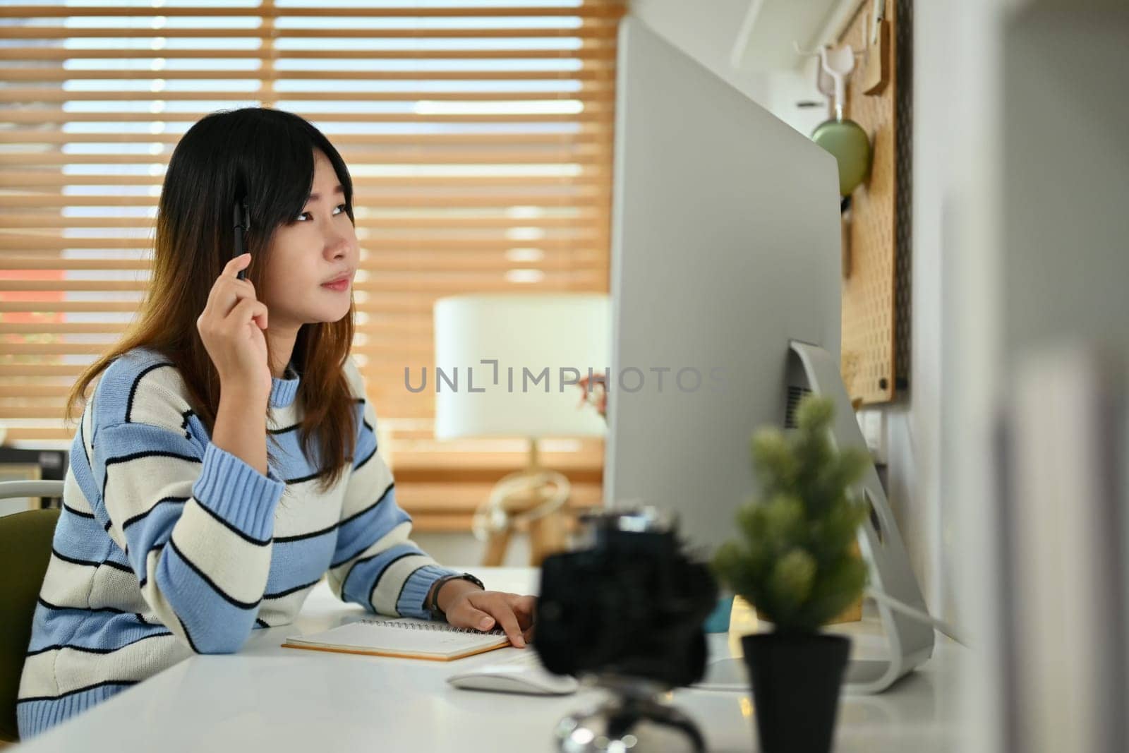 Focused young Asian woman using computer at home office.