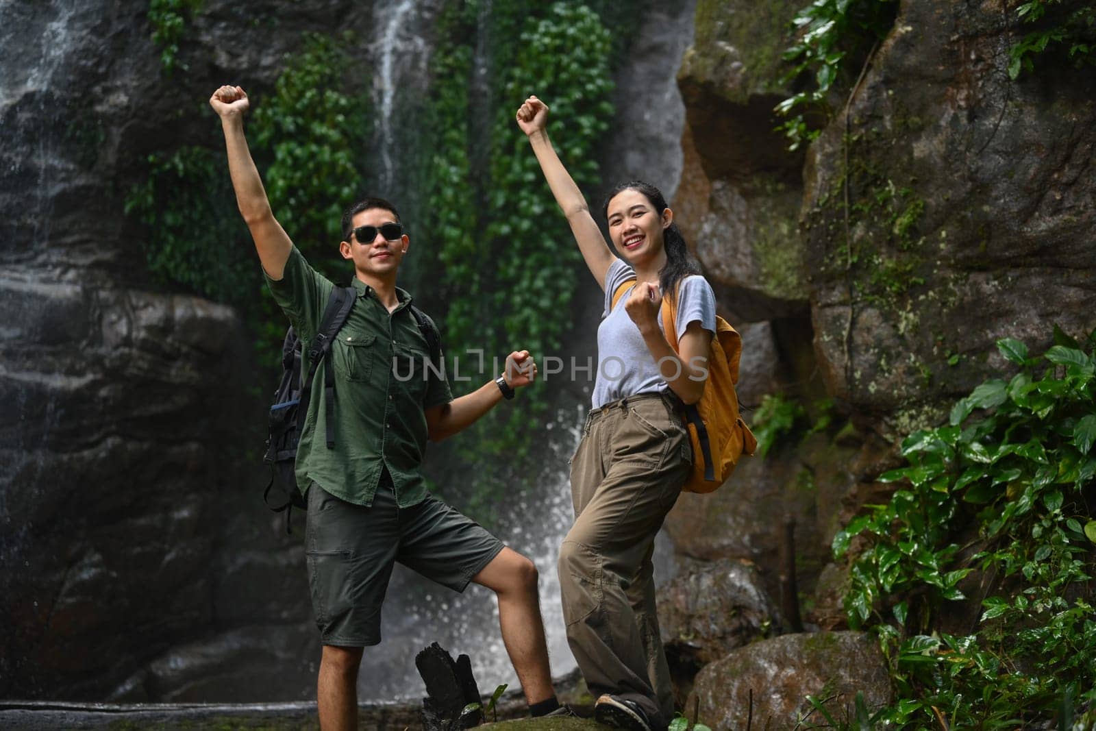 Young couple tourist raising hand to celebrating achievement, success and goal in forest by prathanchorruangsak