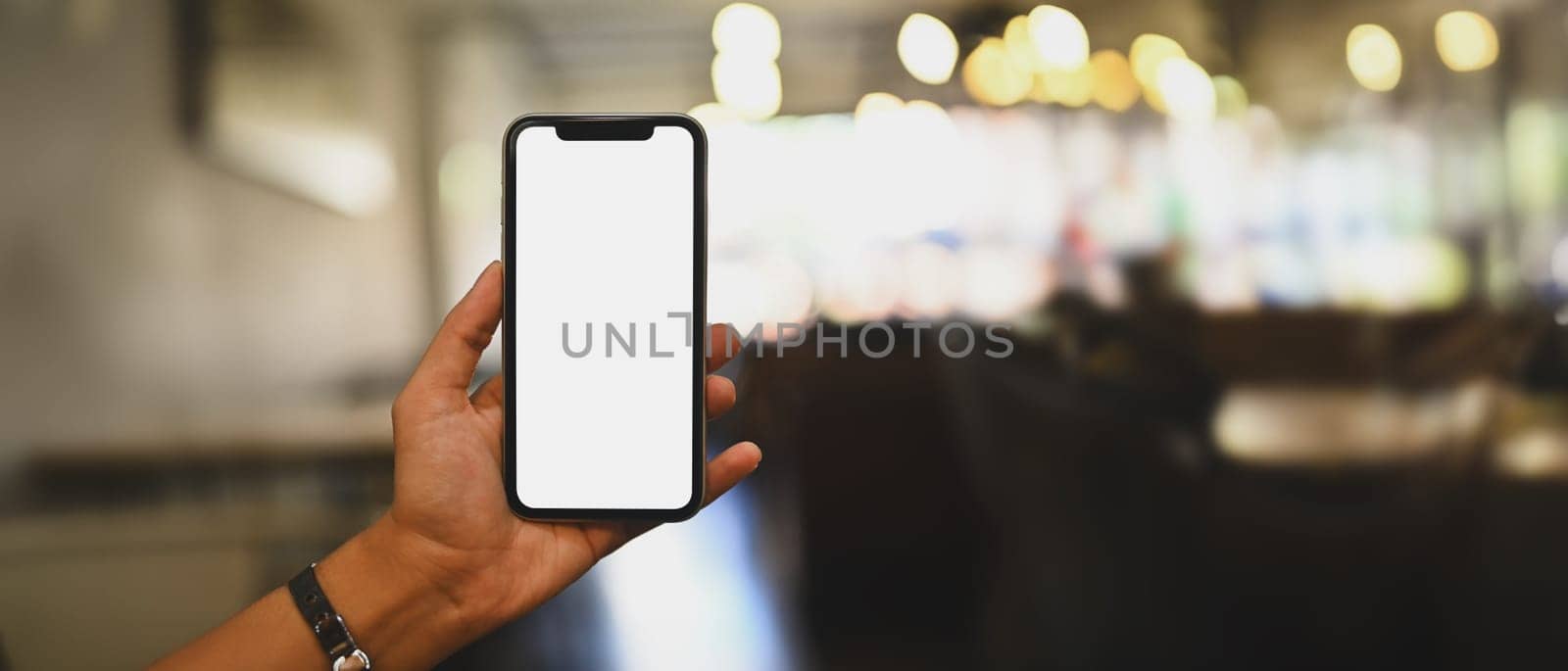 Woman hand holding mobile phone with blurred restaurant on background. Blank screen for your advertise design.