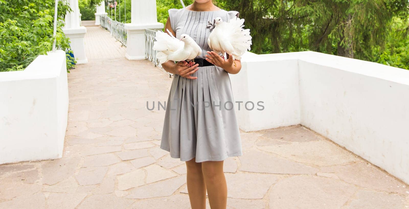 young woman holding a white pigeons in her hands on background outdoor.