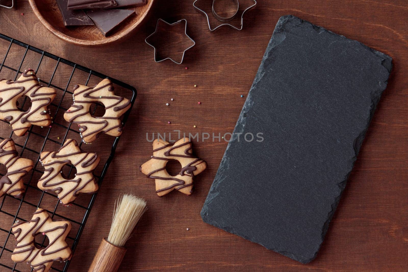 Black stone slate plate with freshly baked homemade star-shaped cookie with chocolate on the grid on the wooden table with a copy space, horizontal banner