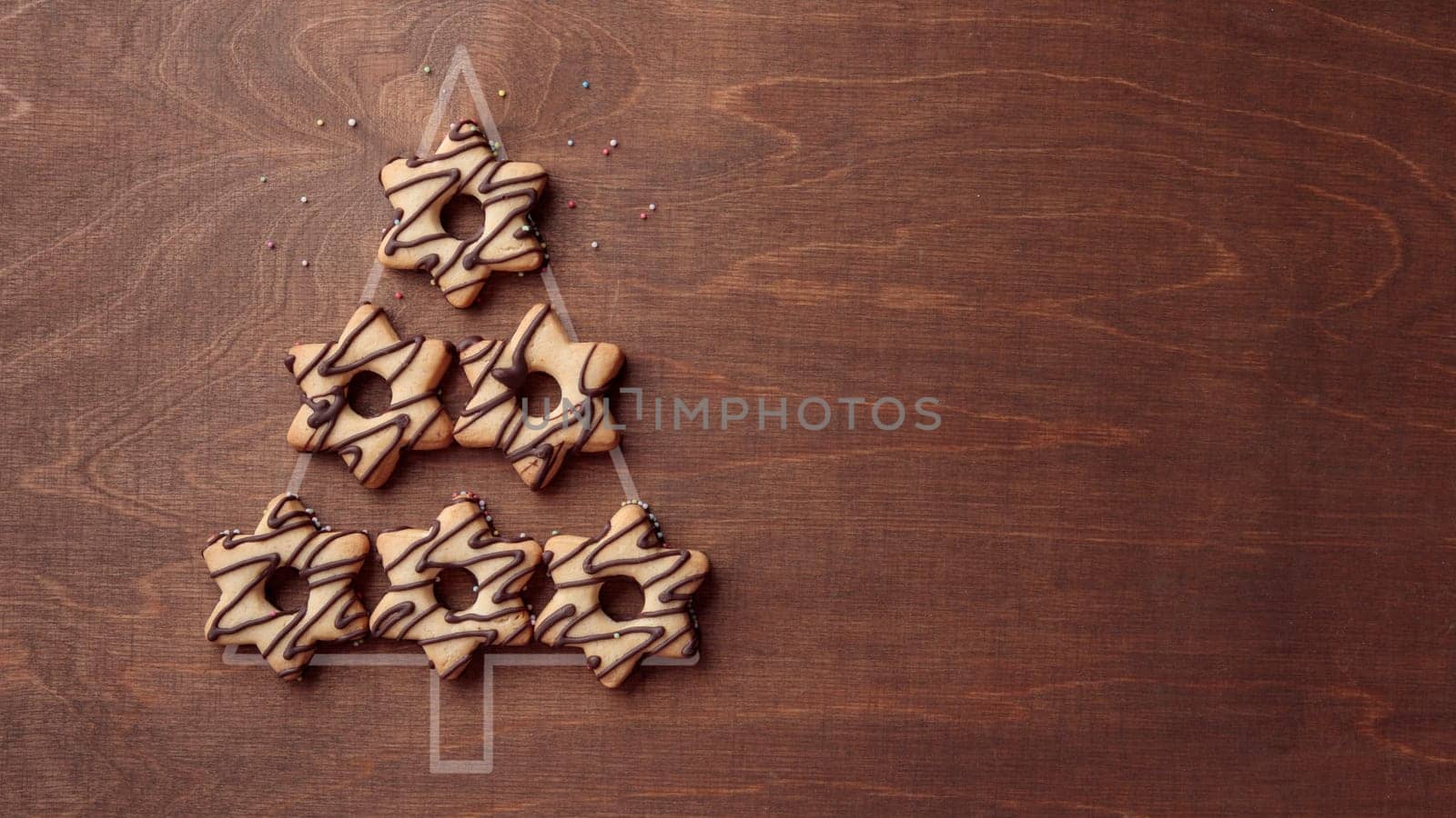 Christmas tree form made from star-shaped cookies with chocolate, banner on the brown wooden background with copy space