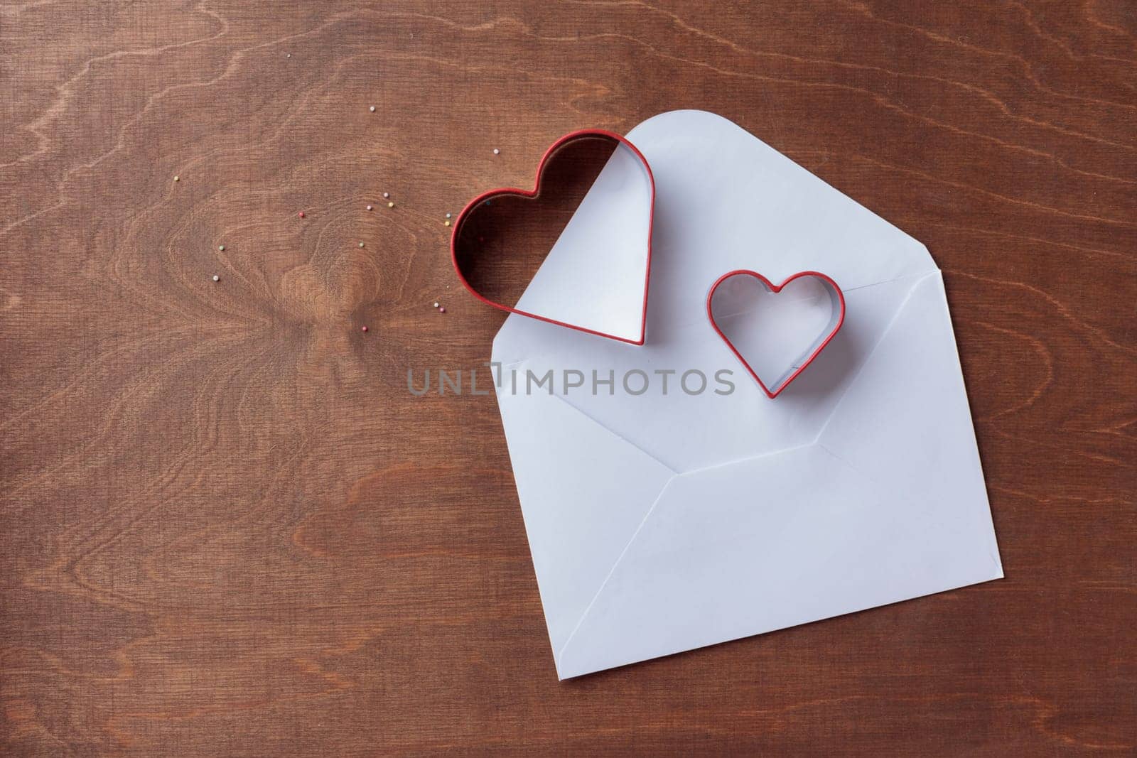 Two heart-shaped cookie cutters on the dark brown wooden background with letter, horizontal banner, top view