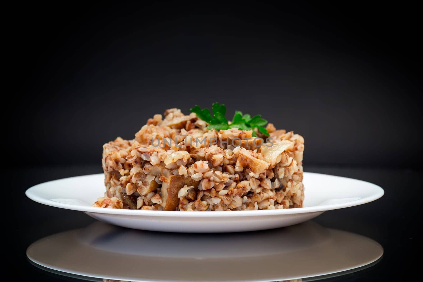 cooked buckwheat boiled with mushroom filling in a plate isolated on a black background.