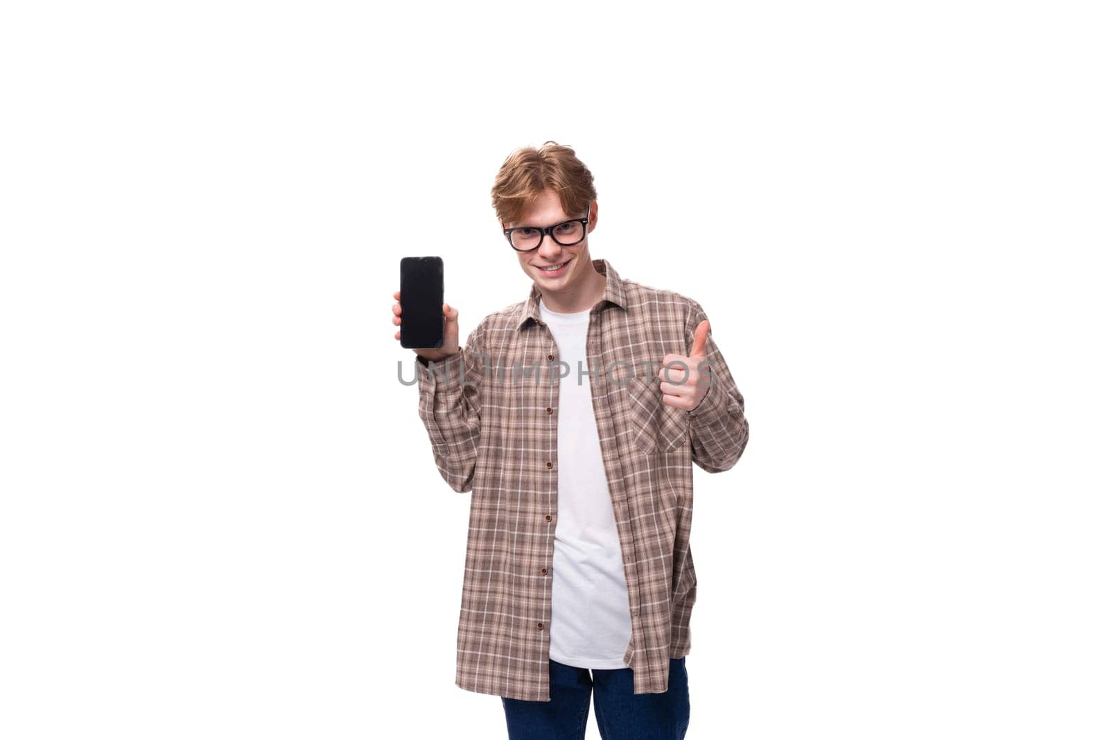 a young caucasian guy with red hair in glasses and a plaid shirt shows the screen of a smartphone. advertising concept.