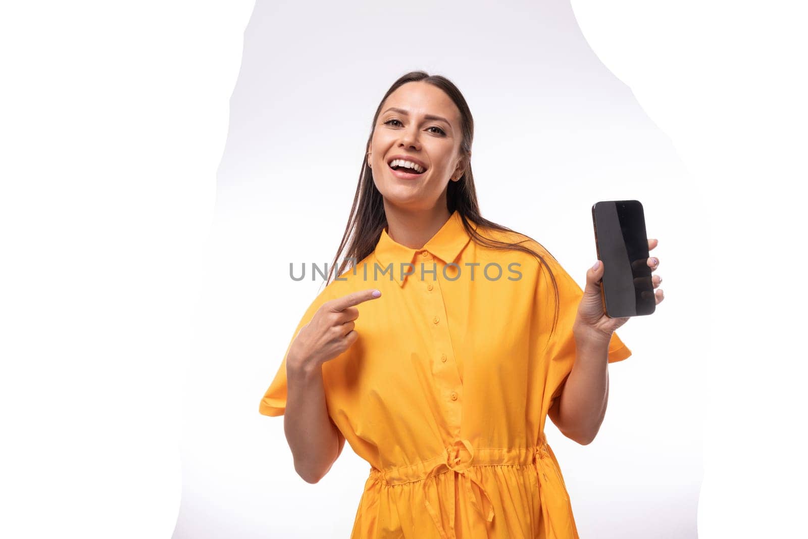 well-groomed slender young brunette lady dressed in a bright yellow short-sleeved dress shows a smartphone screen with a mockup by TRMK