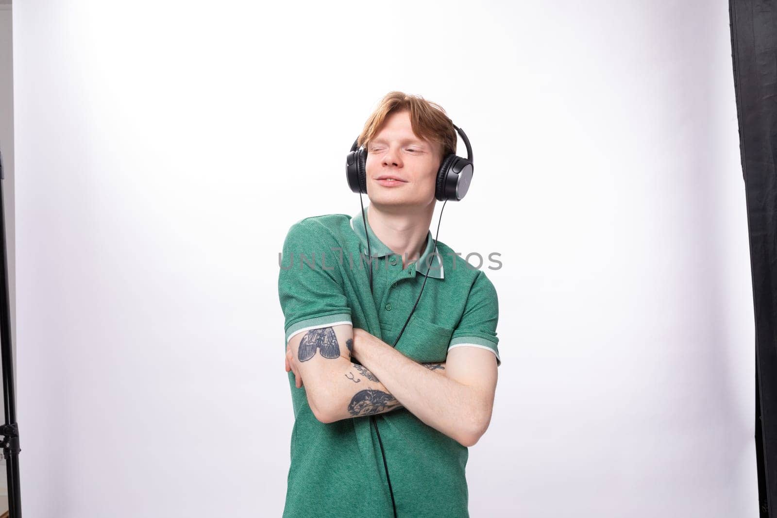 young handsome red-haired man in a green t-shirt enjoys and gets high from listening to music in headphones.