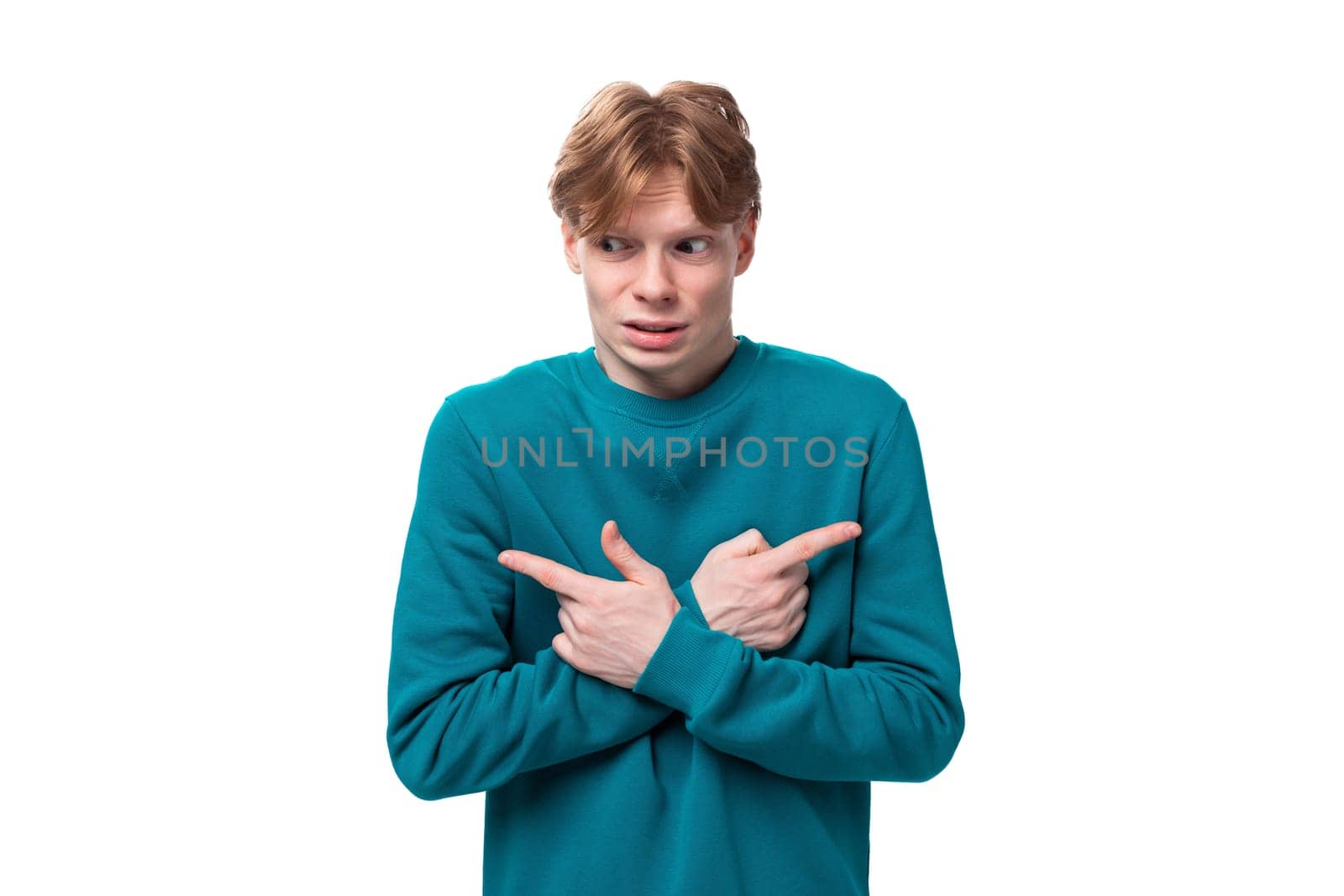 young handsome red-haired man with a blue sweater points his finger at the advertising space.