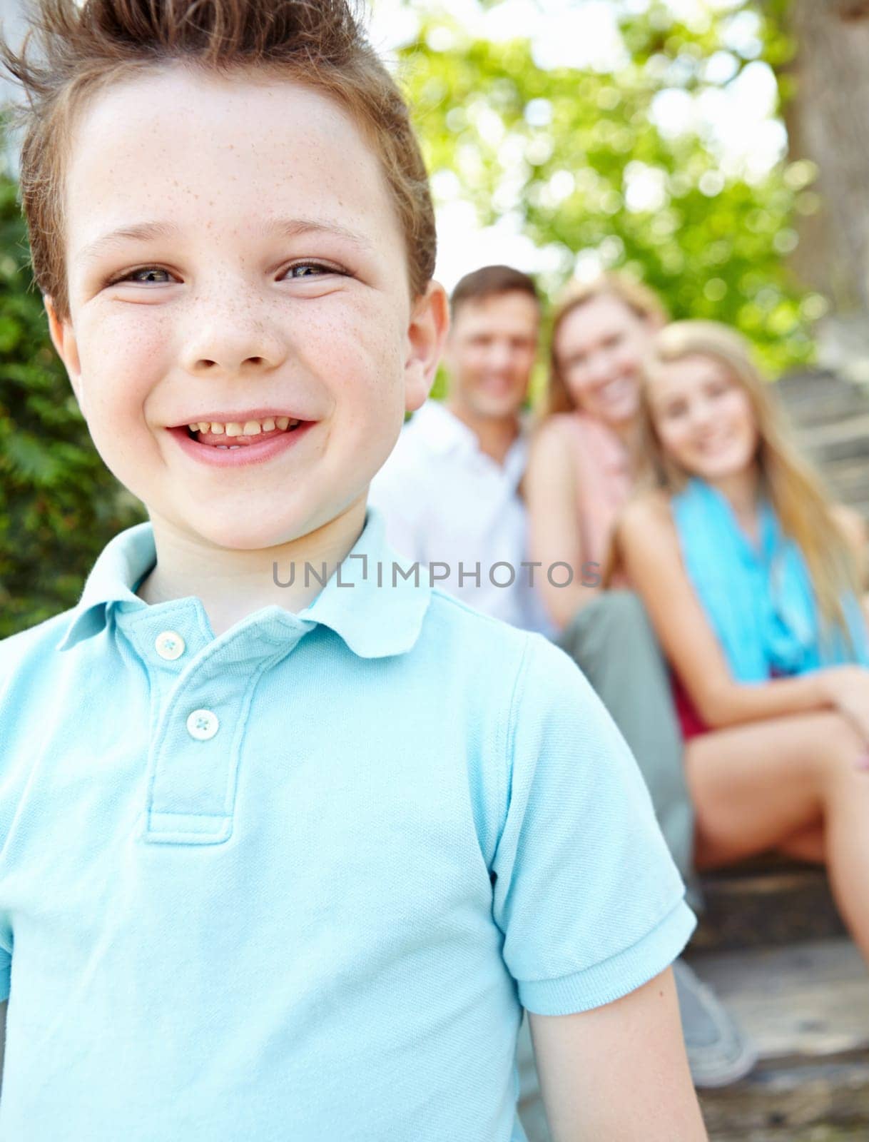 This is my family. Cute little boy with family sitting behind him while outdoors