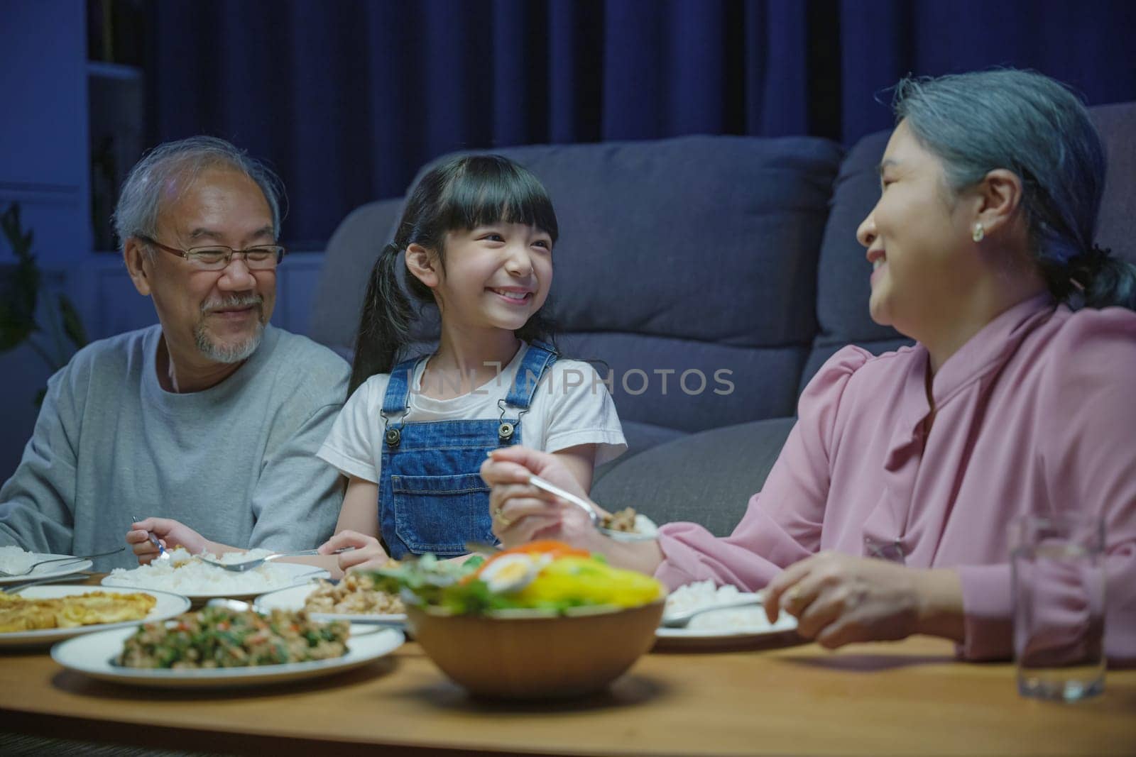 Happy Asian family grandparent and granddaughter dining on table and having fun during at house evening time, Happiness senior parent and child eating dinner food together in living room indoors