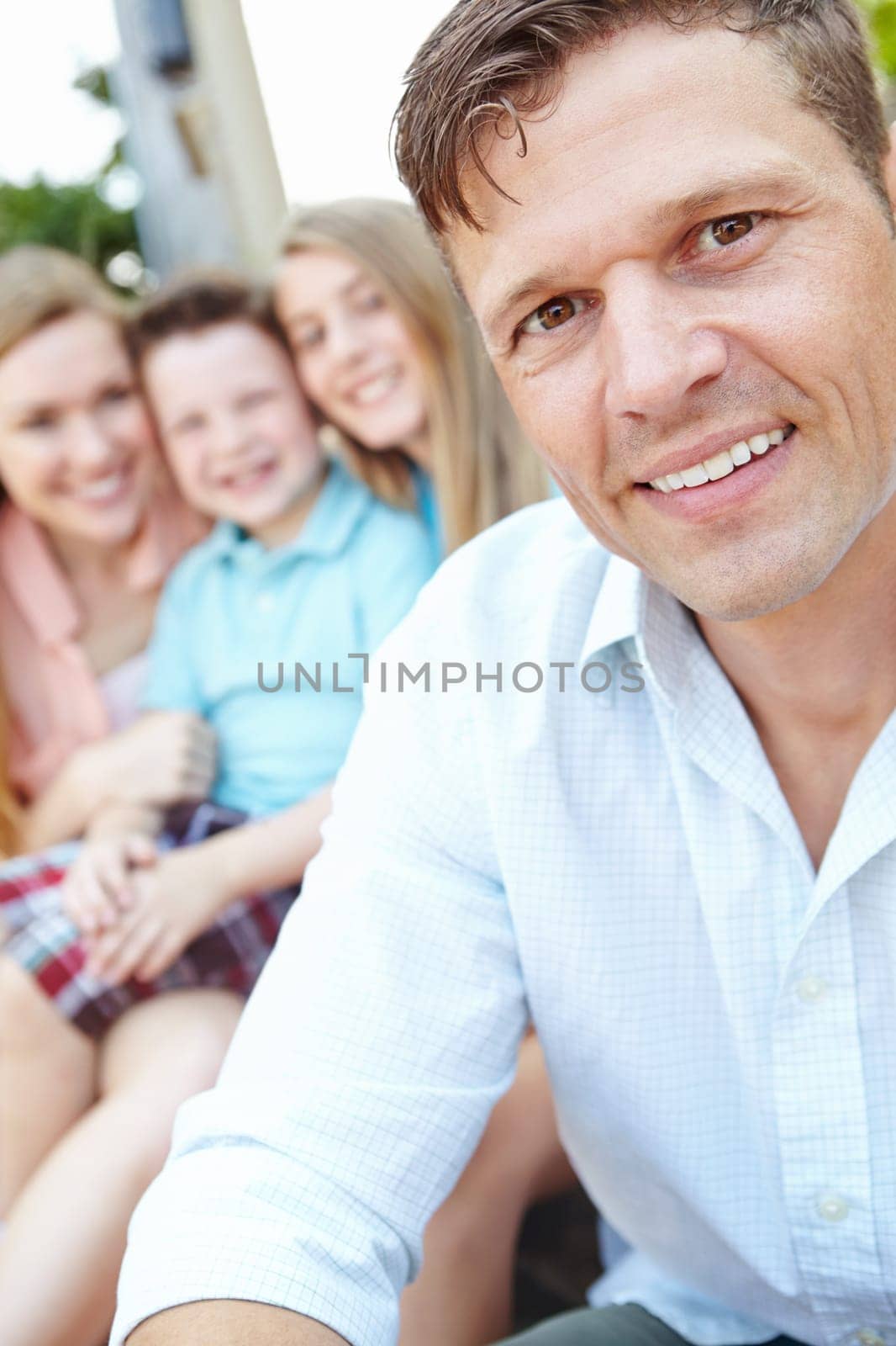 We are a close knit family. Handsome father with family sitting behind him while outdoors