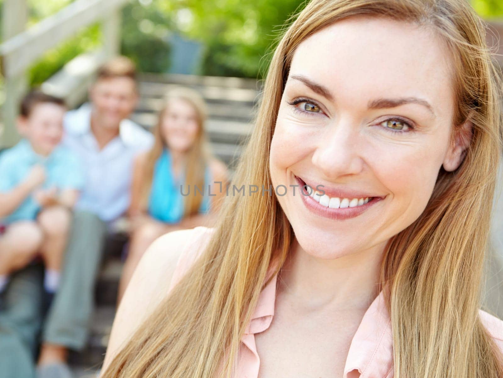 The family matriarch. Smiling attractive mother with family sitting behind her while outdoors