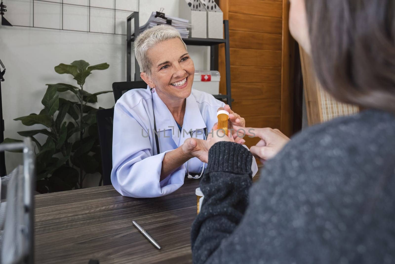 Elderly female doctor in white coat talking with beautiful young patient in clinic, giving advice on heart disease treatment and health care and medicine, medicine concept.