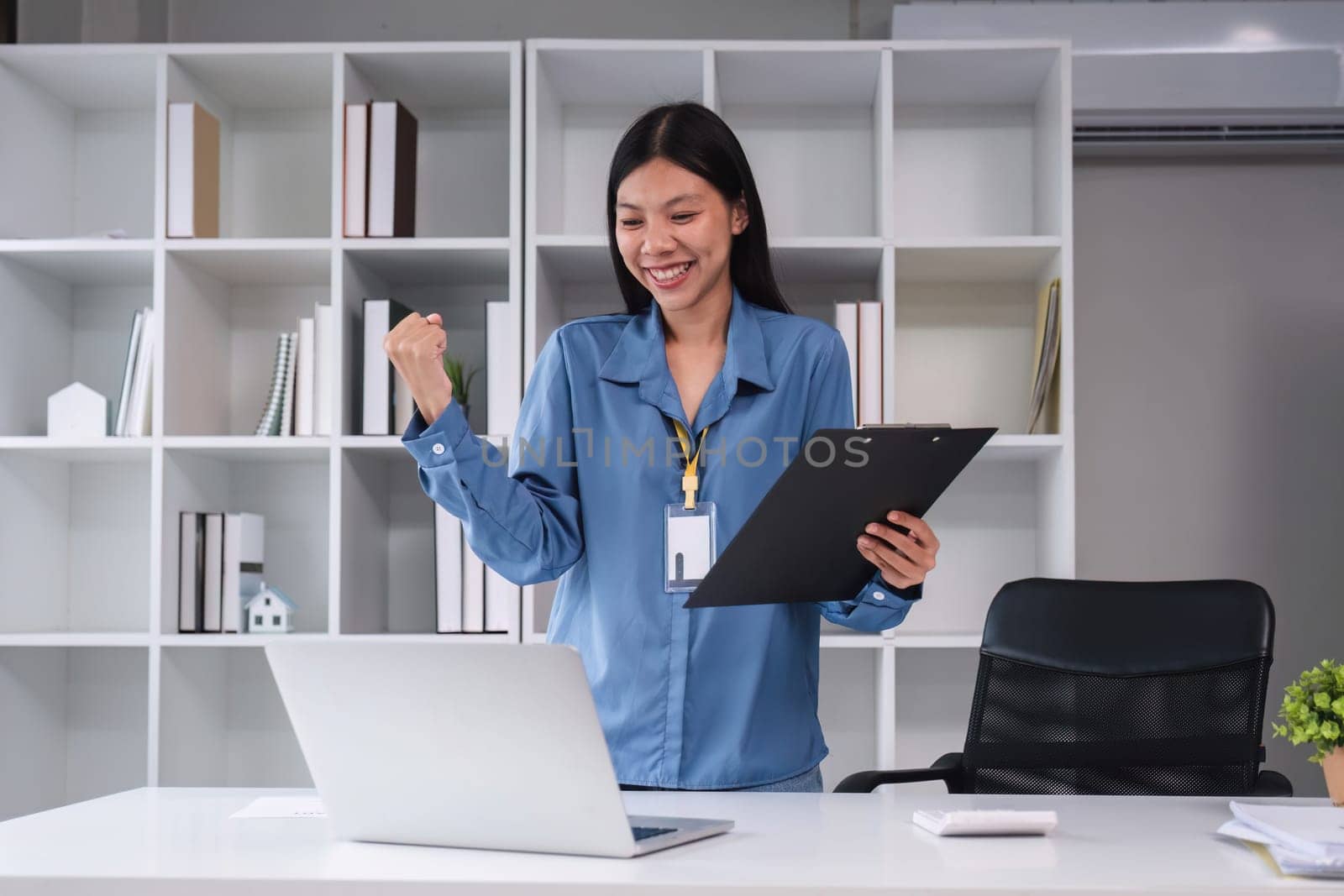 Businesswoman shows joy holding math clipboard on wooden table in office and business background, tax, accounting, statistics and analytical research concept..