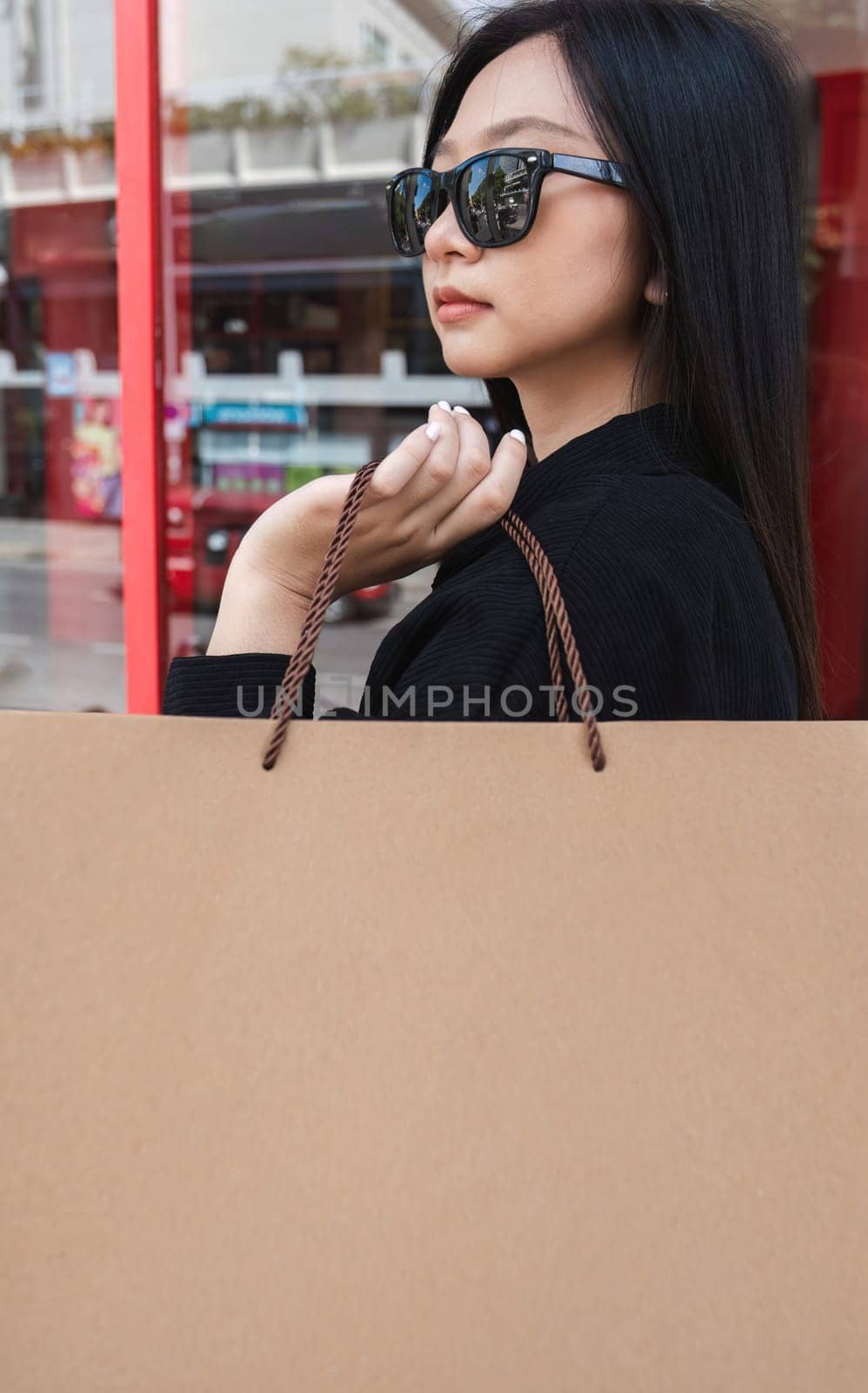 Side view of young Asian woman holding shopping bags on Black Friday while standing in the mall area copy space by wichayada