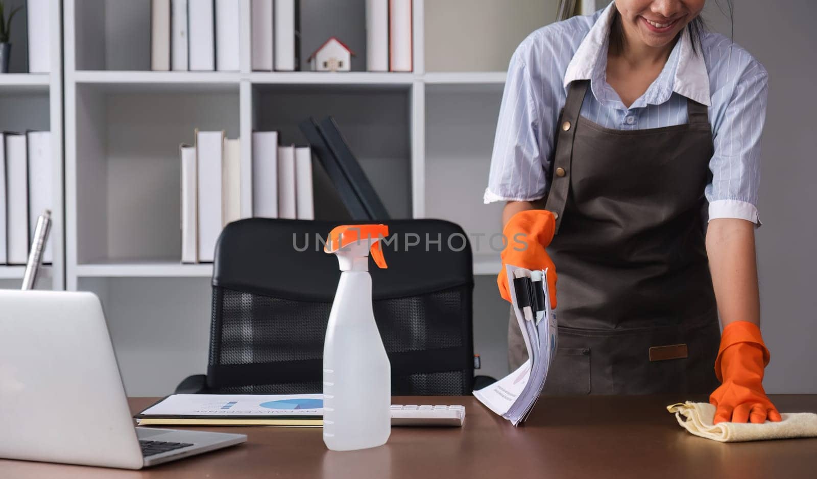 Young woman uses a cleaning cloth to disinfect the computer and equipment on the office table. Cleaning worker or housekeeper cleans the office by wichayada