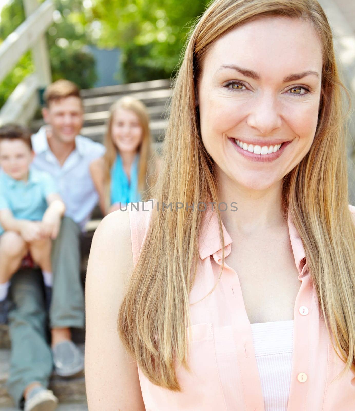 Im one proud mom. Smiling attractive mother with family sitting behind her while outdoors. by YuriArcurs