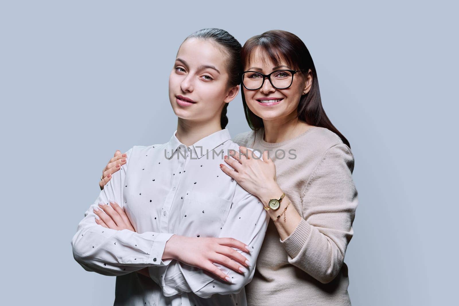 Portrait of middle aged mother and teenage daughter embracing together on grey studio background. Smiling happy mom and girl looking at camera. Family, lifestyle, relationship, mother's day concept
