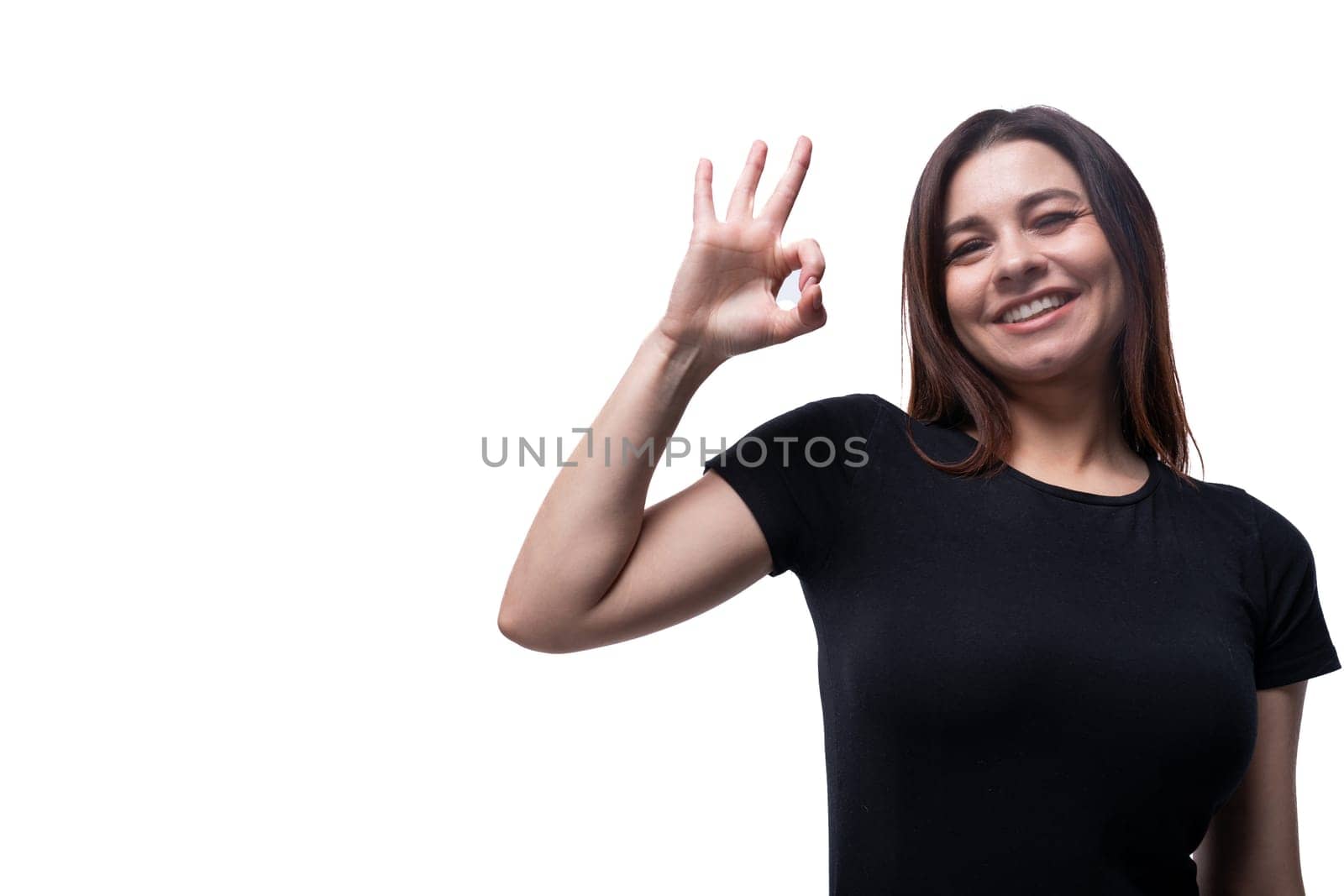 Caucasian cute young woman with black hair dressed in a black t-shirt gesturing on a white background with copy space.