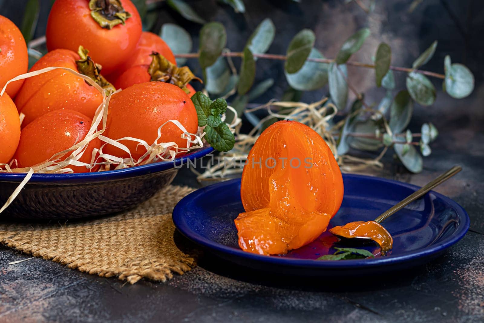 Persimmon on a dark background. Fresh, ripe fruits on a blue plate and in a box. Healthy eating.