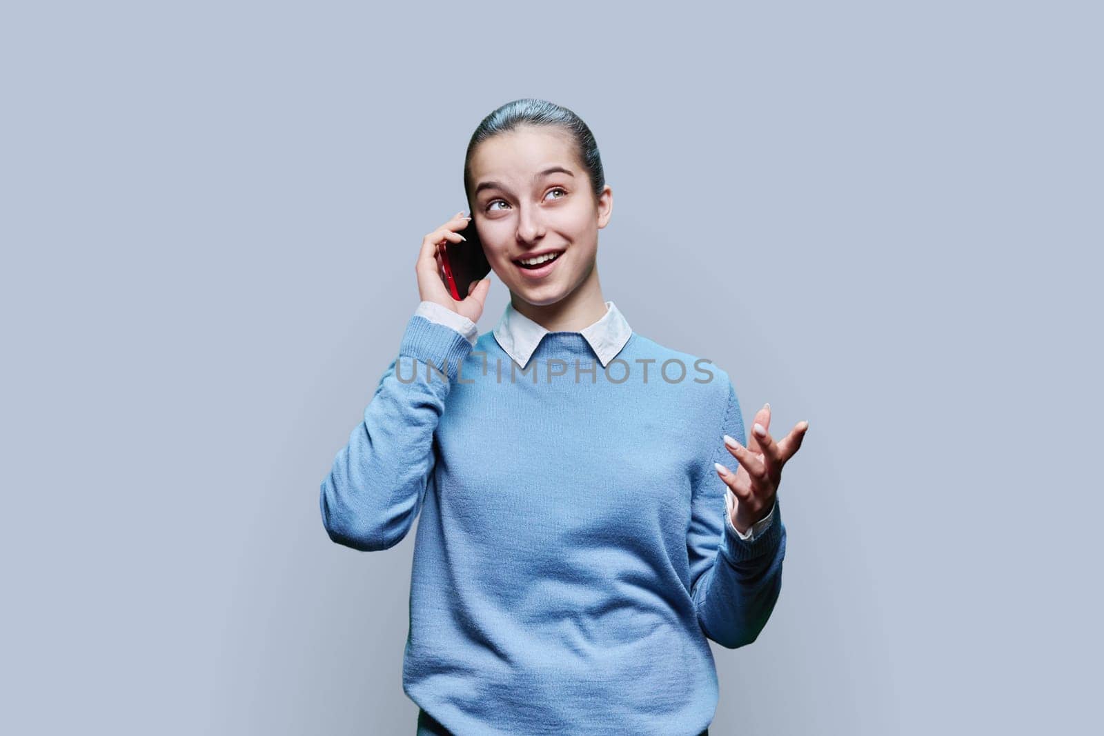 Joyful teenage student girl talking on mobile phone on gray background by VH-studio