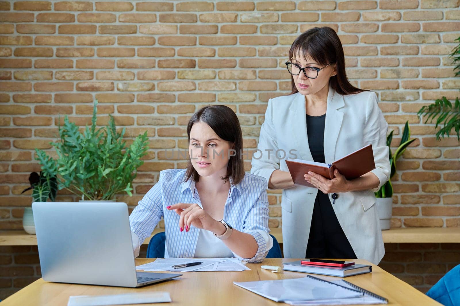 Two businesswomen talking and discussing in office. Female colleagues, manager and employee analyze and discuss documents, contracts, financial reports. Work law finance teamwork people job concept