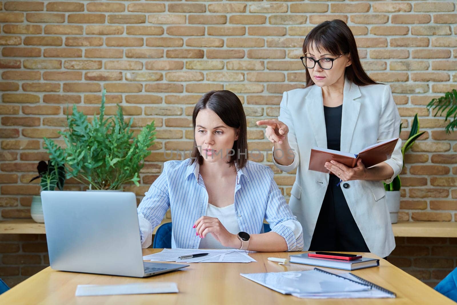 Two businesswomen talking and discussing in office. Female colleagues, manager and employee analyze and discuss documents, contracts, financial reports. Work law finance teamwork people job concept