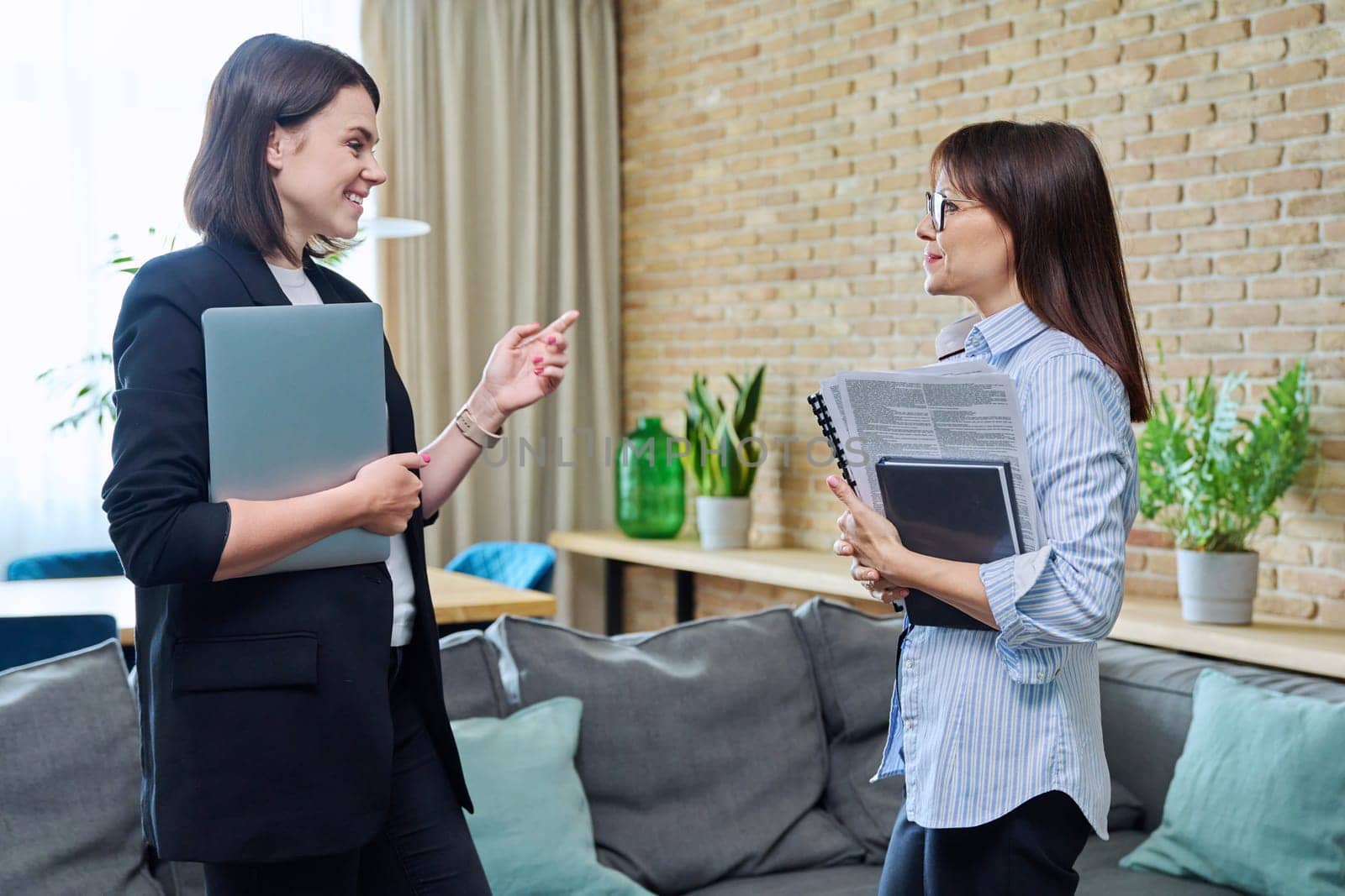 Two businesswomen talking and discussing in office. Female colleagues, manager and employee analyze and discuss documents, contracts, financial reports. Work law finance teamwork people job concept