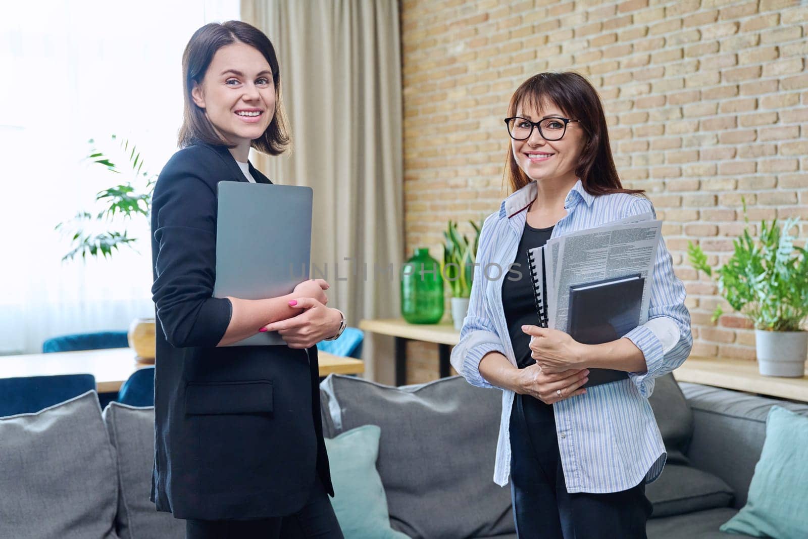 Two smiling business women looking at camera in office by VH-studio