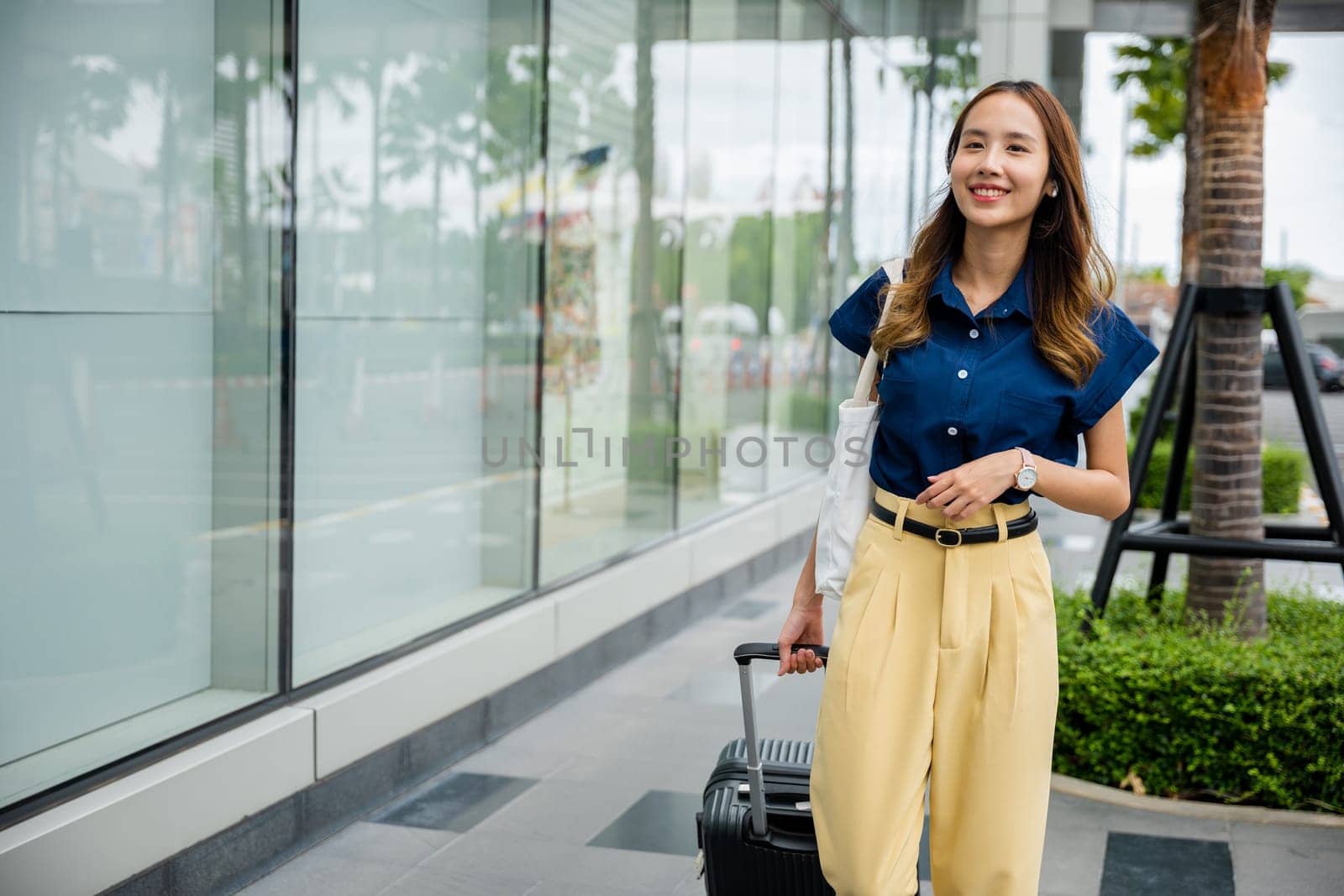 A black businesswoman smiles as she walks down a city street with her luggage and smartphone, ready for her next adventure.