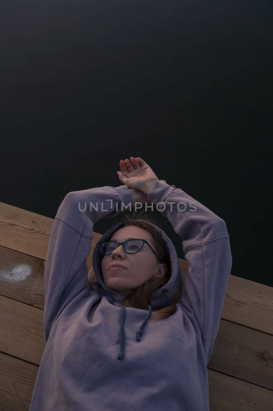 Woman lying down on the pier at lake, closeup portrait, summer sunset
