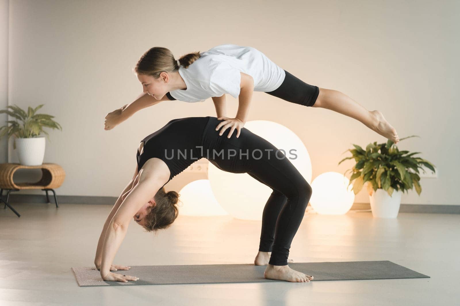 Mom and teenage daughter do gymnastics together in the fitness room. A woman and a girl train in the gym by Lobachad