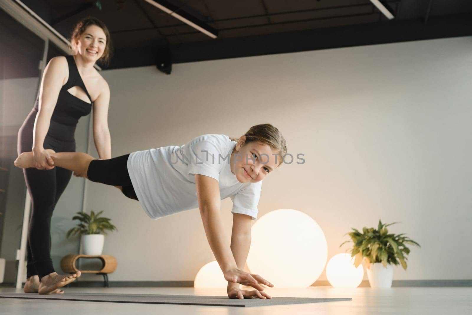 Mom and teenage daughter do gymnastics together in the fitness room. A woman and a girl train in the gym by Lobachad