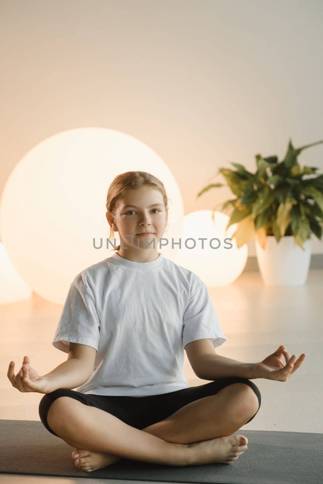 A teenage girl in sports clothes does yoga in a fitness room.